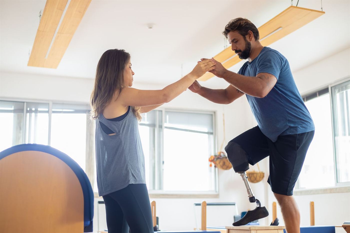 A man with a prosthetic leg practicing a balance exercise while holding hands with his physical therapist